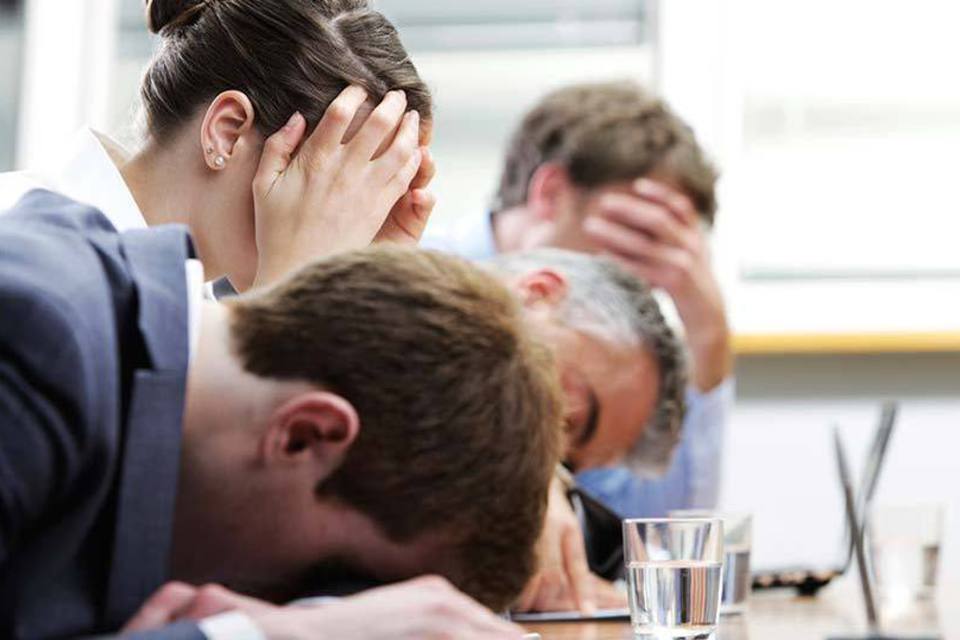 Várias pessoas estão debruçadas sobre uma mesa, como se estivessem exaustas