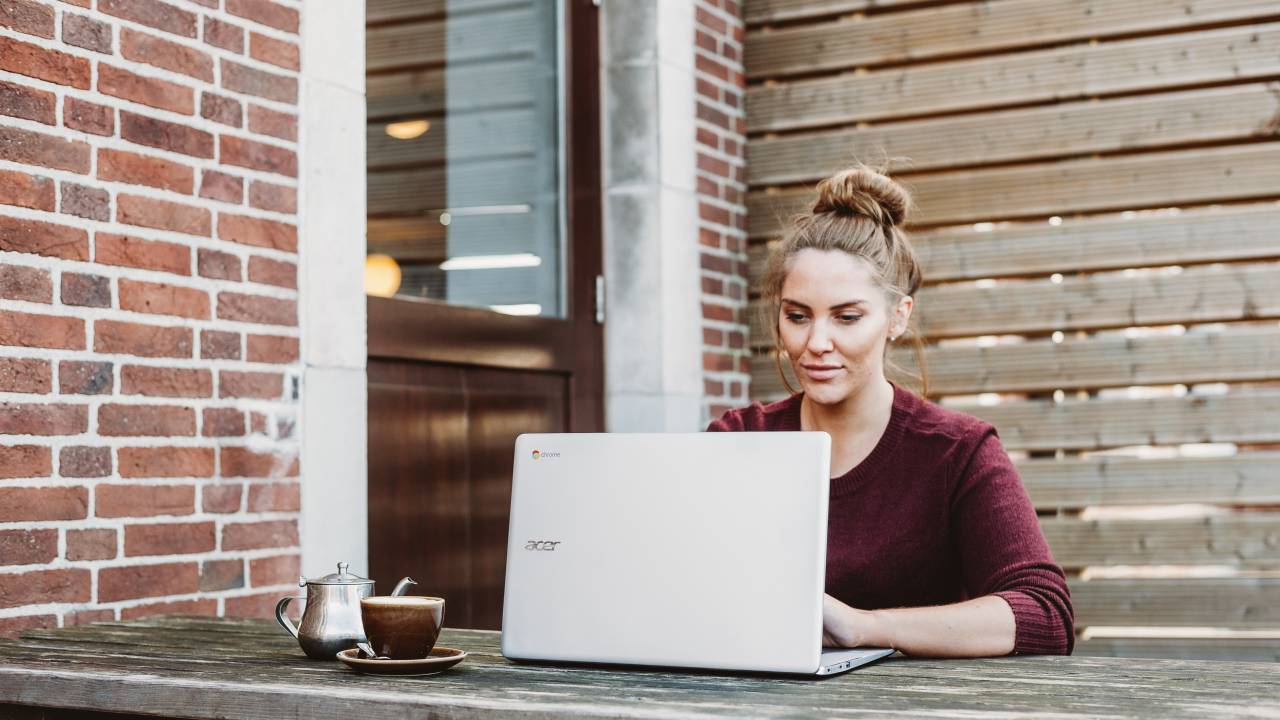 Mulher usando o notebook em uma mesa ao ar livre.