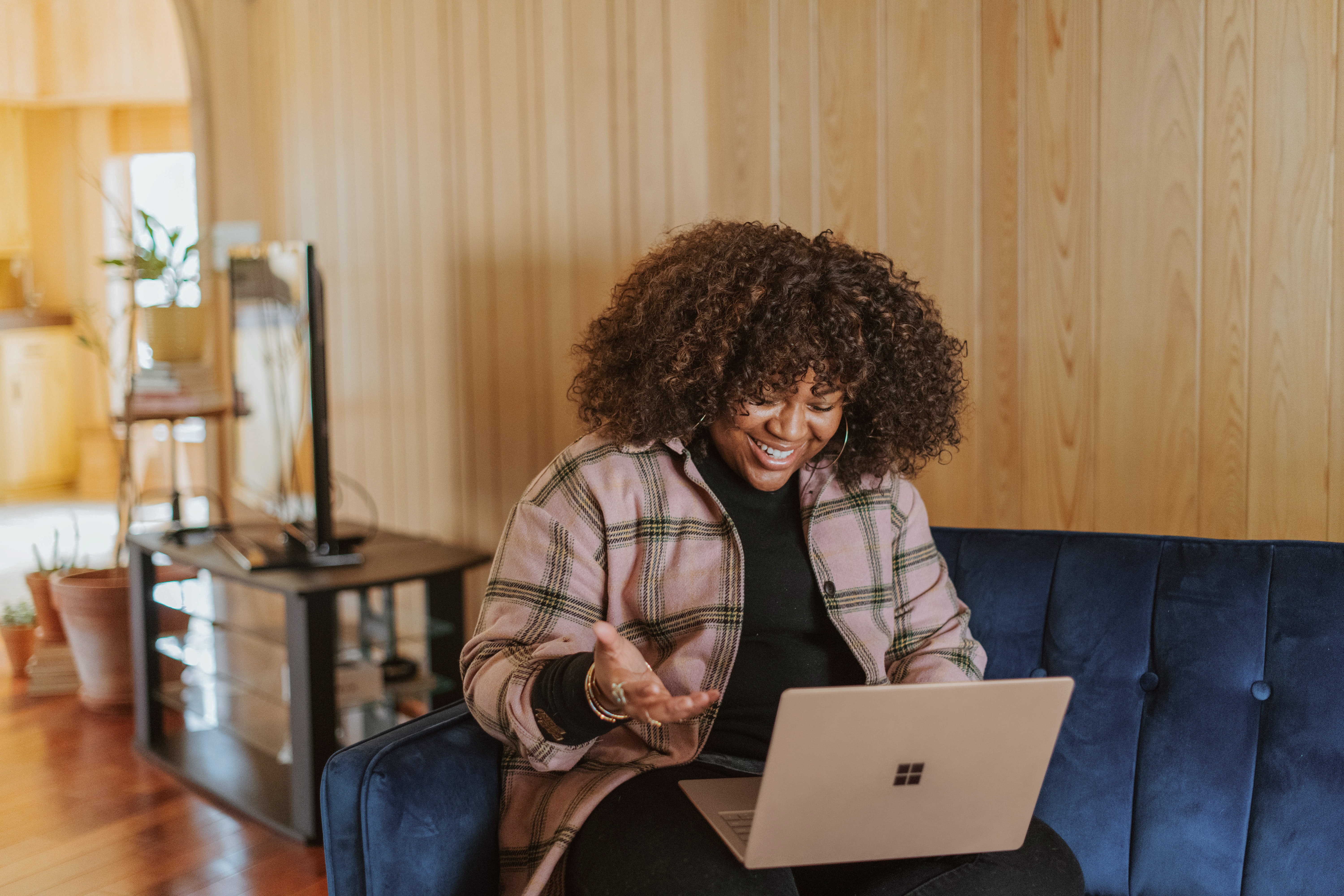 Imagem mostra mulher negra sentada em um sofá com notebook no colo em uma videoconferência