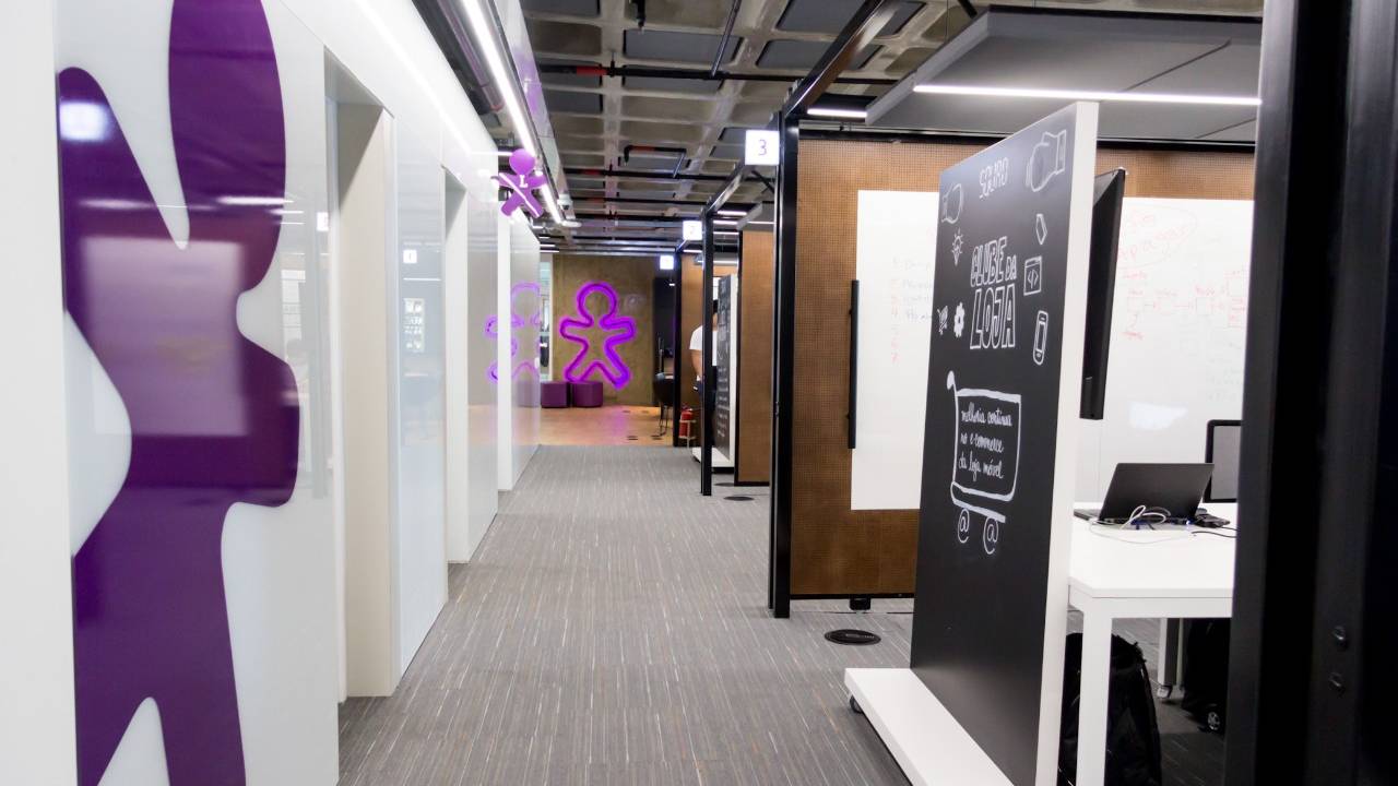 Imagem mostra o escritório da Vivo, com o símbolo da empresa em roxo nas paredes.