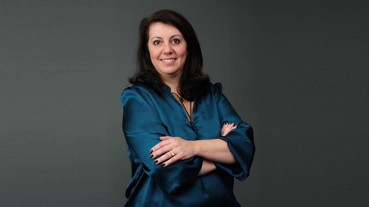 Foto de Beatriz Sairafi, uma mulher branca, de cabelos escuros e camisa azul.