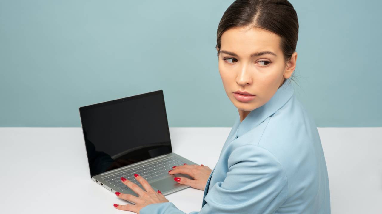 Uma mulher está trabalhando, com as mãos sobre o teclado de seu notebook, enquanto olha para trás, assustada