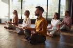 Imagem de jovem empresário e seus colegas exercitando Yoga em posição de Lótus no chão do escritório