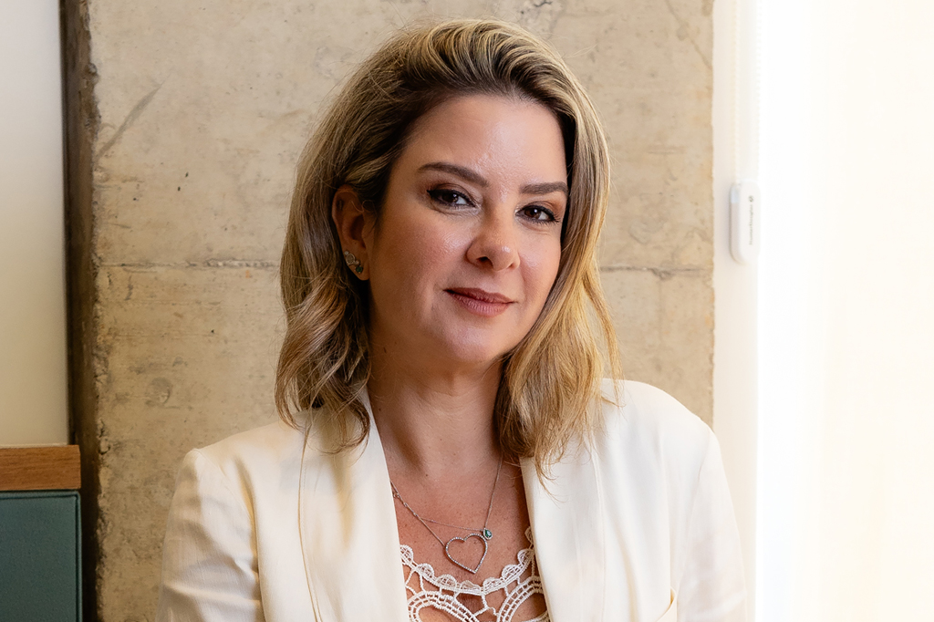 Foto de mulher sorrindo, vestindo terno branco.