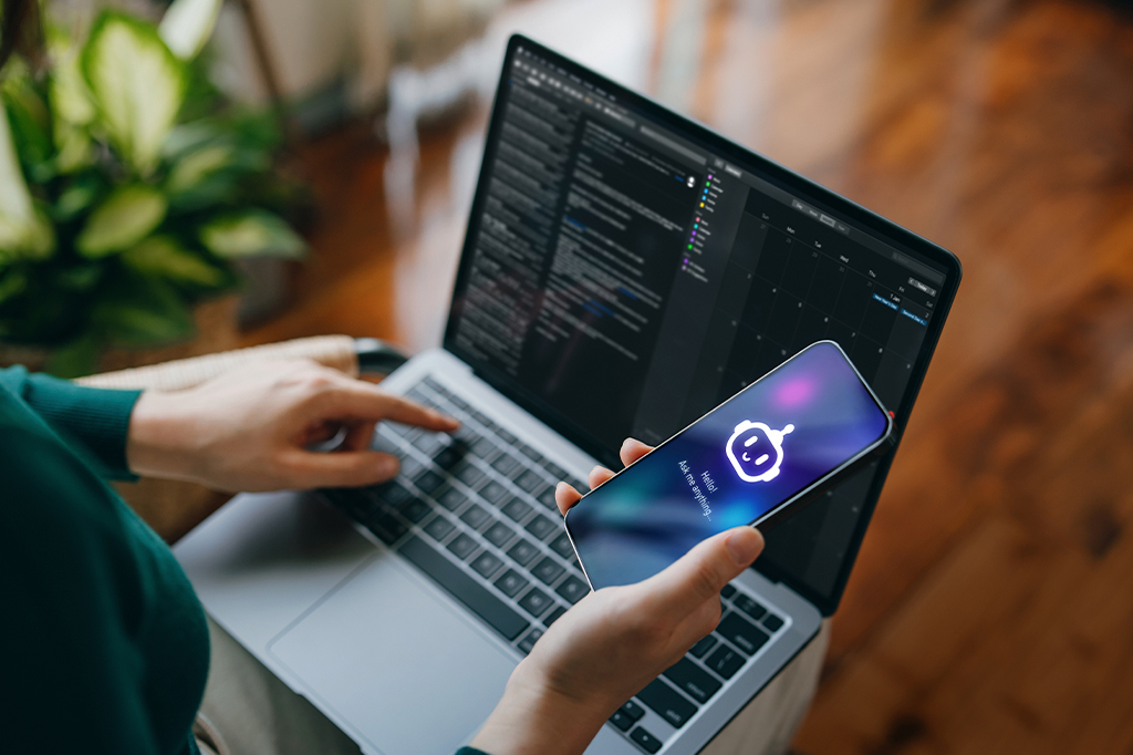 Fotografia de um mulher usando aplicativo de assistência virtual de chatbot de IA no smartphone para ajudá-la enquanto trabalha no laptop.