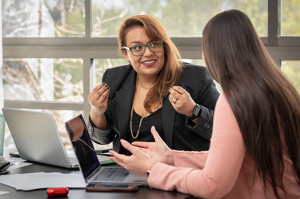 Fotografia de duas mulheres conversam alegremente enquanto trabalham em seus laptops.