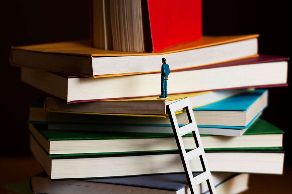 Miniatura de um homem acima de uma pilha de livros.