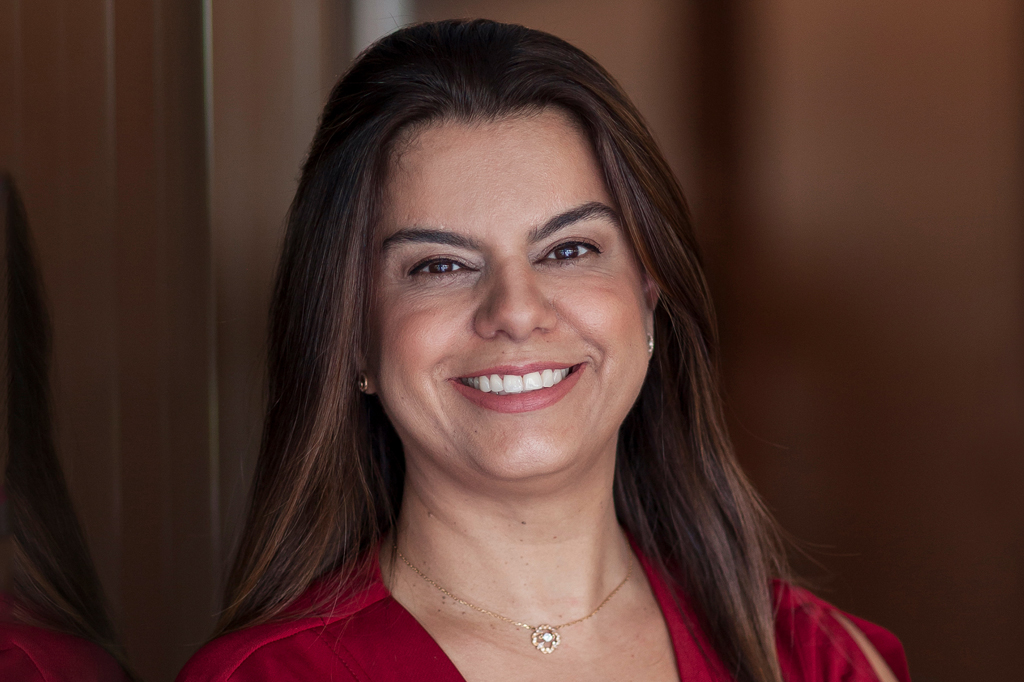 Imagem de uma mulher jovem, sorrindo, de cabelos longos e usando um vestido vermelho carmim.
